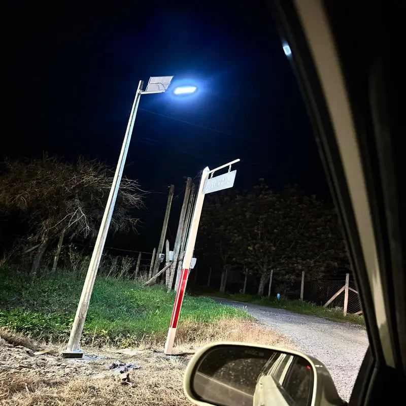 Foco solar LED 1500W instalado en camino rural, iluminando el acceso a una parcela de noche